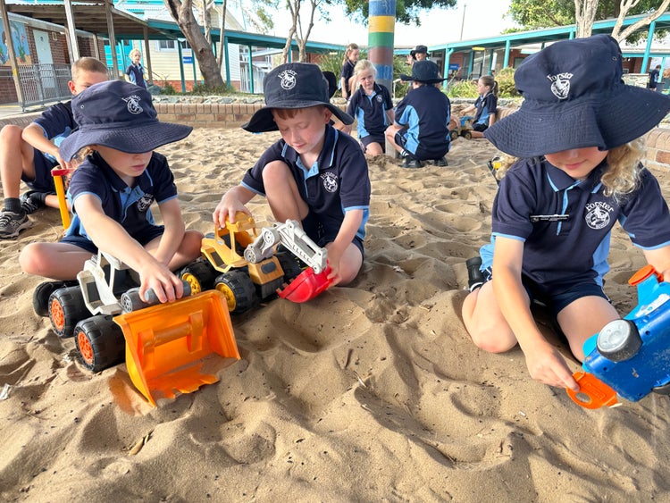 group of students playing with toy trucks in a sandpit