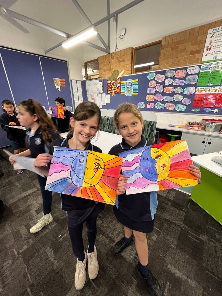 Two girls holding paintings in the classroom