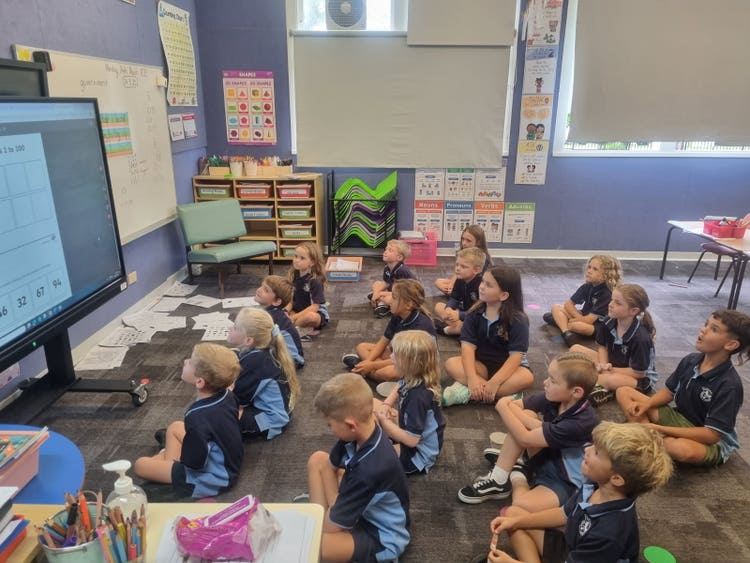 students sitting on the floor in classroom looking at the whiteboard