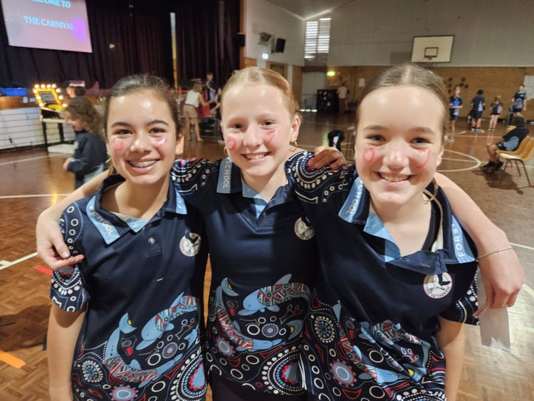 three girls with arms around each other smiling in school hall